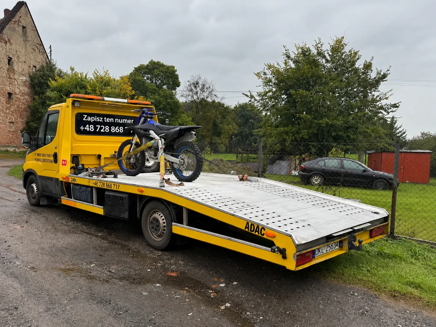 Laweta z motocyklem crossowym przypiętym pasami do platformy